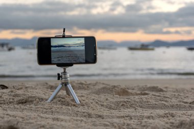 Cep telefonu plajda gün batımını çekerken tripoda takılı kalmış.).