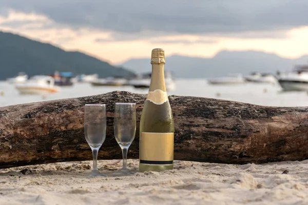 Sahilde köpüklü şarap pençesi, iki cam kasenin yanında, arka planda bir ağaç gövdesi..