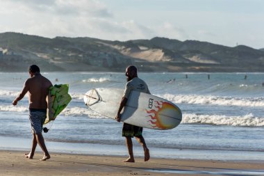 Natal, Ponta Negra Sahili, Rio Grande do Norte, Brezilya, 27 Temmuz 2019: Öğleden sonra Ponta Negra plajında yürüyen iki usta sörfçü.