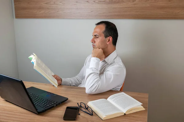 43 year old man holding book and concentrating, resting his chin on his closed hand.