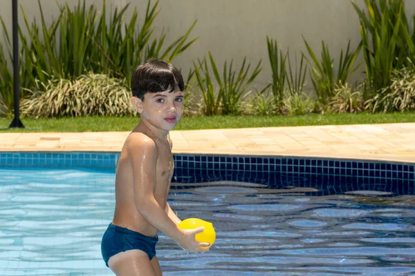 6 yaşında bir çocuk, eli ağzında ve su bombasını tutuyor..