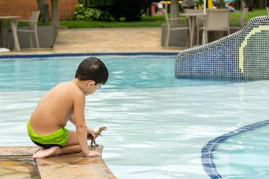 6 yaşında bir çocuk, sırtı havuzun kenarında dinozorla oynuyor..