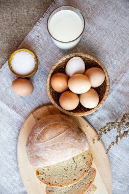 Ekmek, süt ve tuz dolu yumurta ve ahşap tabaklarda, arka planda sıcak renklerde..
