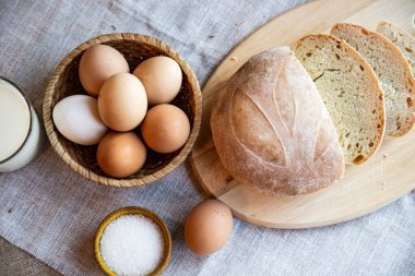 Ekmek, süt ve tuz dolu yumurta ve ahşap tabaklarda, arka planda sıcak renklerde..