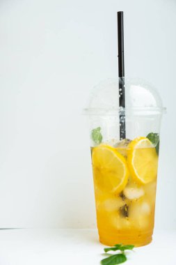 Beyaz arka planda plastik bardakta buzlu limon ve limon kremi ile yeşil çay.