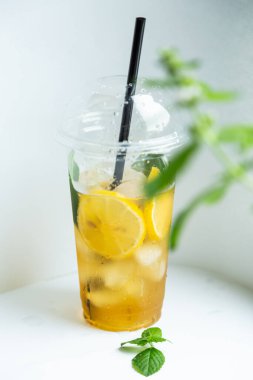 Beyaz arka planda plastik bardakta buzlu limon ve limon kremi ile yeşil çay.