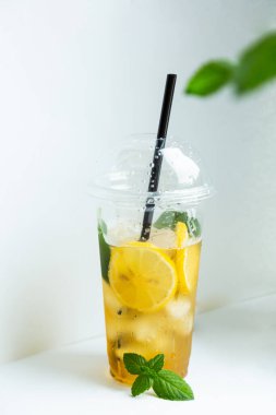 Beyaz arka planda plastik bardakta buzlu limon ve limon kremi ile yeşil çay.