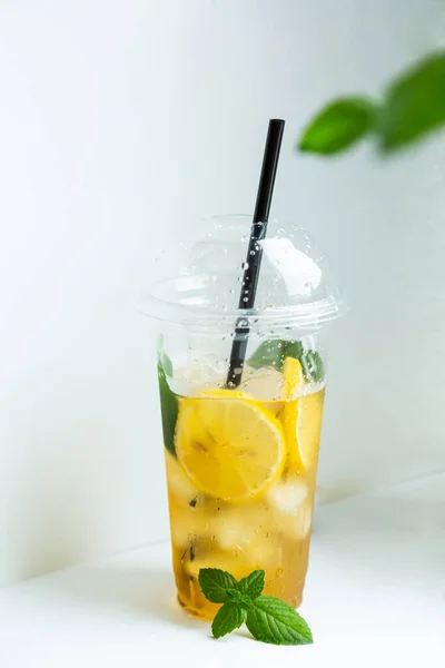 Beyaz arka planda plastik bardakta buzlu limon ve limon kremi ile yeşil çay.