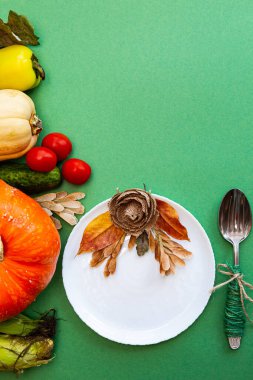 Sonbahar yapraklı beyaz tabak ve çatal bıçak takımı ve yeşil arka planda sebzeler. Şenlikli sonbahar konsepti.