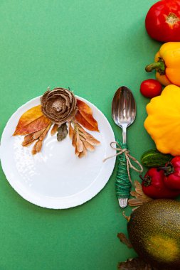Sonbahar yapraklı beyaz tabak ve çatal bıçak takımı ve yeşil arka planda sebzeler. Şenlikli sonbahar konsepti.