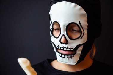 İskelet gibi giyinmiş bir çocuk elinde bir kafatası lolipopu tutuyor.