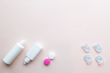 Kontak lensler, lens solüsyonu ve açık pembe arka planda lens kapları. Sağlık konsepti üst görünüm kopyalama alanı