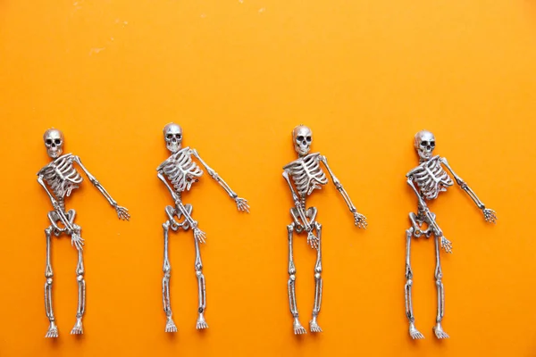 Skeletons in silver and gold are dancing on an orange background. Halloween and Day of the Dead concept — Stock Image Skeletons Silver Gold Dancing Orange Background Halloween Day Dead Concept Royalty Free Stock Photos