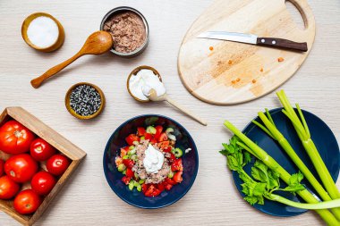 Kerevizli salata, domates ve ton balığı. Hafif ahşap masa manzaralı yemek pişirme sürecinde salata malzemeleri.