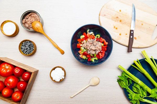 Kerevizli salata, domates ve ton balığı. Hafif ahşap masa manzaralı yemek pişirme sürecinde salata malzemeleri.