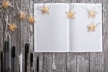 Noel çelengi, boş kare defter ve gri tahta bir masada kalemler. Noel dilek listesi. Metin için kopyalama alanı olan planlayıcı