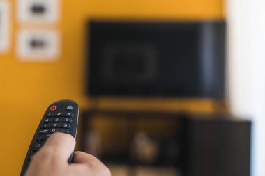 Oturma odasında televizyon izlemek için uzaktan kumandayı tutuyorum.