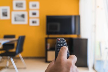 Oturma odasında televizyon izlemek için uzaktan kumandayı tutuyorum.