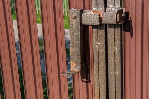 Rusty deadbolt for an entrance gate made of metal picket, in the open state.