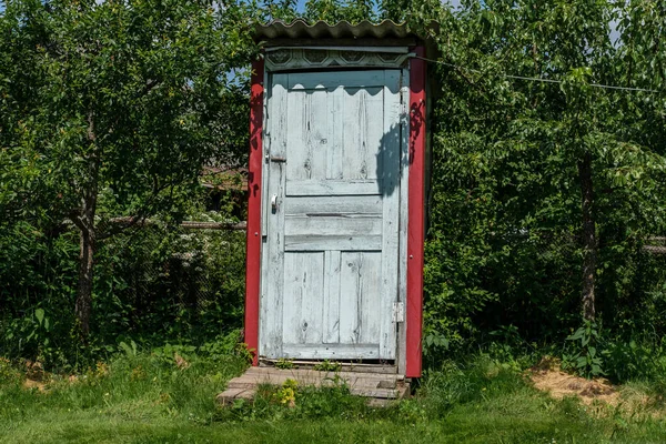 A rustic toilet stands sunlit on a street among fruit trees. — Stock Image Rustic Toilet Stands Sunlit Street Fruit Trees Stock Image