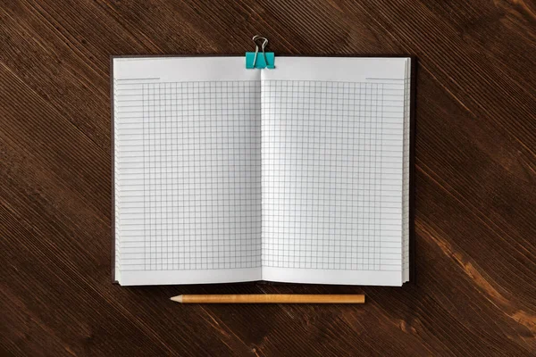 A notebook with squared paper for notes and a light-colored pencil lie on a textured dark wooden table.