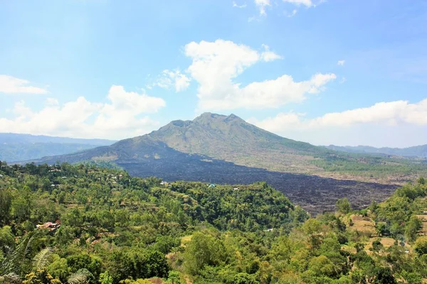 Batur Volkanı Dağı, ağaçlar ve yeşil yapraklarla ön planda ve Bali, Endonezya 'daki siyah volkanik kaya alanıyla