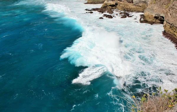 Waves crashing on rocks in clear blue ocean water in Nusa Penida, Indonesia