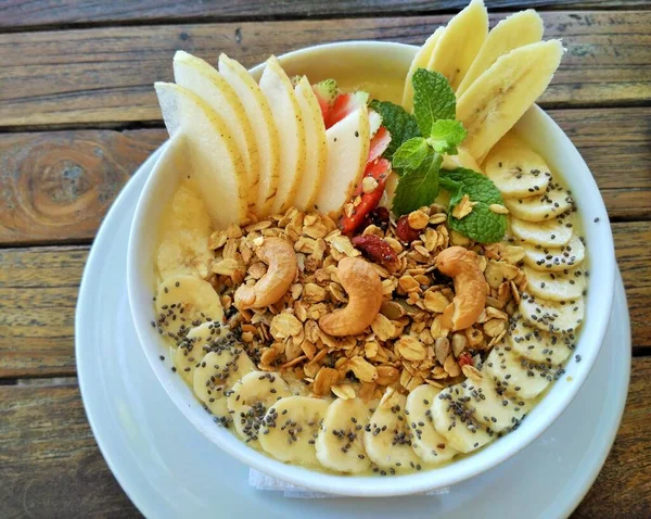 Taze muz, Asya armudu, kaju fıstığı, chia tohumu, granola ve ahşap masa arkasında bir tutam nane aromalı sağlıklı meyve suyu.