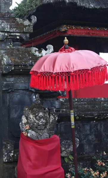 Balijská Socha Pokrytá Červeným Materiálem Vedle Červeného Deštníku Před Stěnou — Stock fotografie