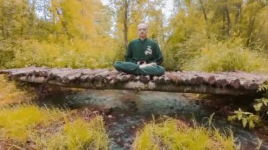 Zaman meditasyonu. Genç bir adam, parlak sarı yapraklarla çevrili ahşap bir köprüde meditasyon yapıyor..