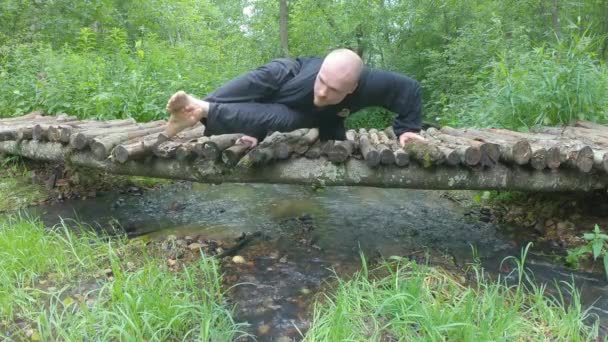 Man Practices Yoga Nature Wooden Bridge Stream Running Clear Sunny — Stock Video