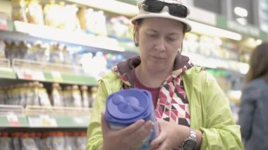 Mağazadaki kadın çocuk için kuru bir karışım seçiyor, ürünün bileşimini dikkatlice okuyor..