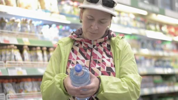Женщина Средних Лет Выбирает Воду Пластиковой Бутылке Внимательно Читай Этикетку — стоковое видео