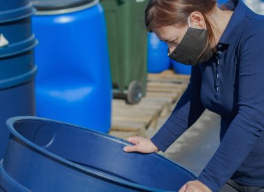 Siyah maskeli bir kadın plastik fıçı seçer. Arkaplan plastik kaplar.