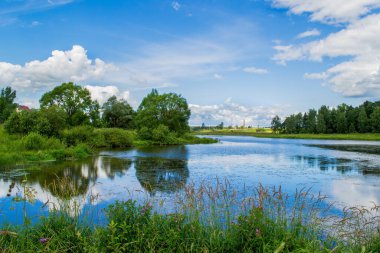 Mavi gökyüzünde süzülen beyaz bulutlar gölün berrak sularında yansıyor.