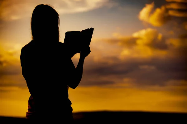女孩读圣经在日落剪影 免版税图库图片