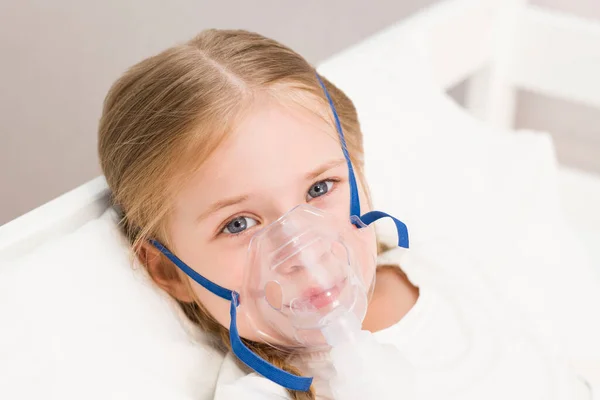 girl is breathing through an inhaler. a sick child is lying on the bed