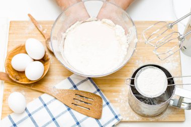 Masanın üzerinde bir kase hamur, un, yumurta, tuz, şeker ve süzgeç var. Pişirme