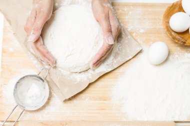 Masanın üzerinde bir kase hamur, un, yumurta, tuz, şeker ve süzgeç var. Pişirme