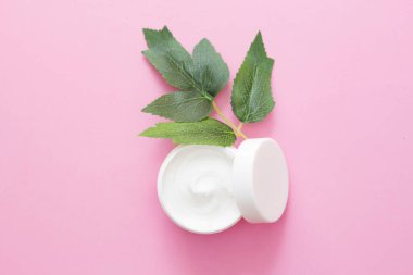 Bir kavanoz yüz kremi, yanında yeşil, egzotik yapraklar olan pembe bir vücut. Doğal Bakım, Organik Krem, Nemlendirici Bakım, Güzellik, Kozmetik Üretimi