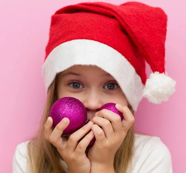 little girl in a red Christmas hat holds Christmas pink balloons in her hands. Close up. Happy new year 2021