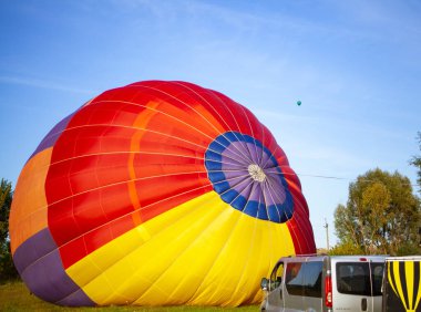 Büyük bir sıcak hava balonu, sarı-kırmızı, parlak renkli, uçuşa hazırlanıyor.