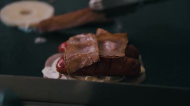 Peynirli sosis ve domuz pastırması ağır çekimde kızartılıyor.