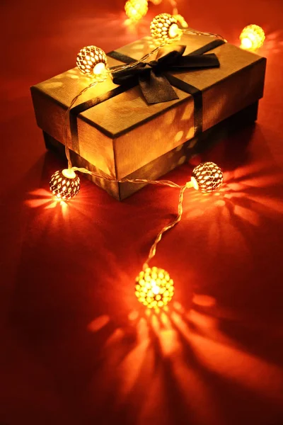 Крупный План Завернутого Подарка Светящимися Рождественскими Огнями Красном Фоне Создавая — стоковое фото