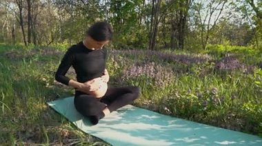 Hamile kadınla çimenlerin üzerinde oturan bebek karnı okşayarak