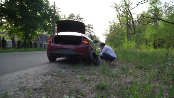 怀孕的女人在车上换了个破轮胎。修理道路上的汽车. — 图库视频影像