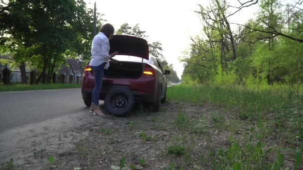 怀孕的女人在车上换了个破轮胎。修理道路上的汽车. — 图库视频影像