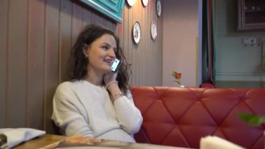 Telefon ve kamera bakar gülümseyen genç kadın konuşuyor. Bir kafede dinlenme.
