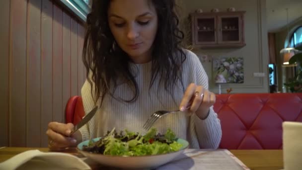 Mujer comiendo ensalada en un café de interior, de cerca en un plato . — Vídeo de stock