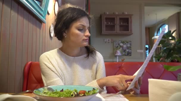 Vrouw naar op zoek is via het menu in restaurant — Stockvideo